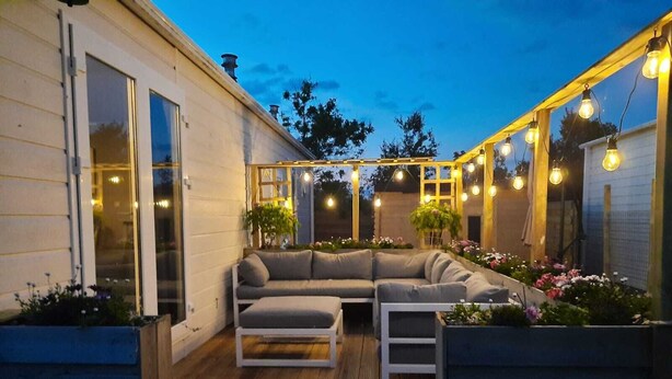 An outdoor patio area with a wooden deck, a gray sectional sofa, and string lights.