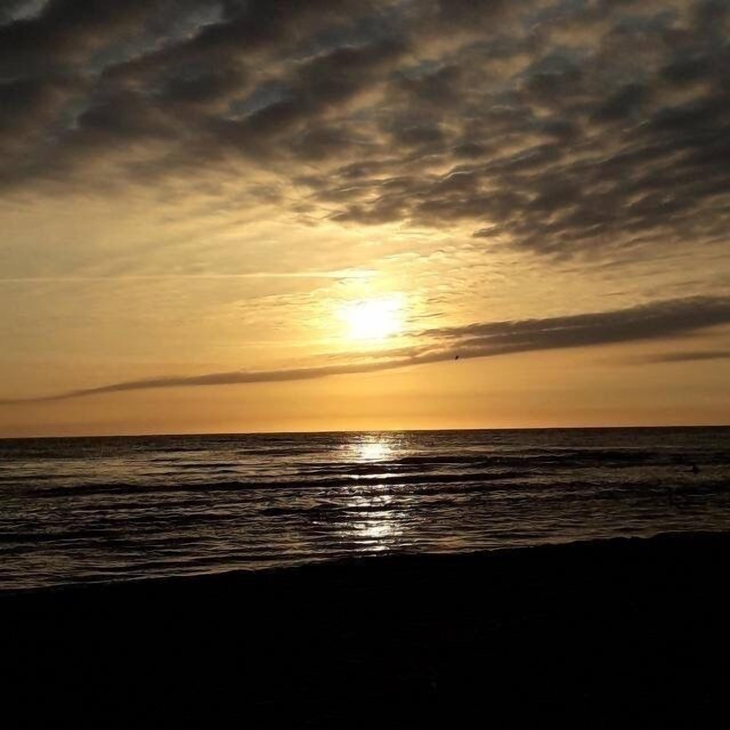 A sunset over the ocean with clouds in the sky.