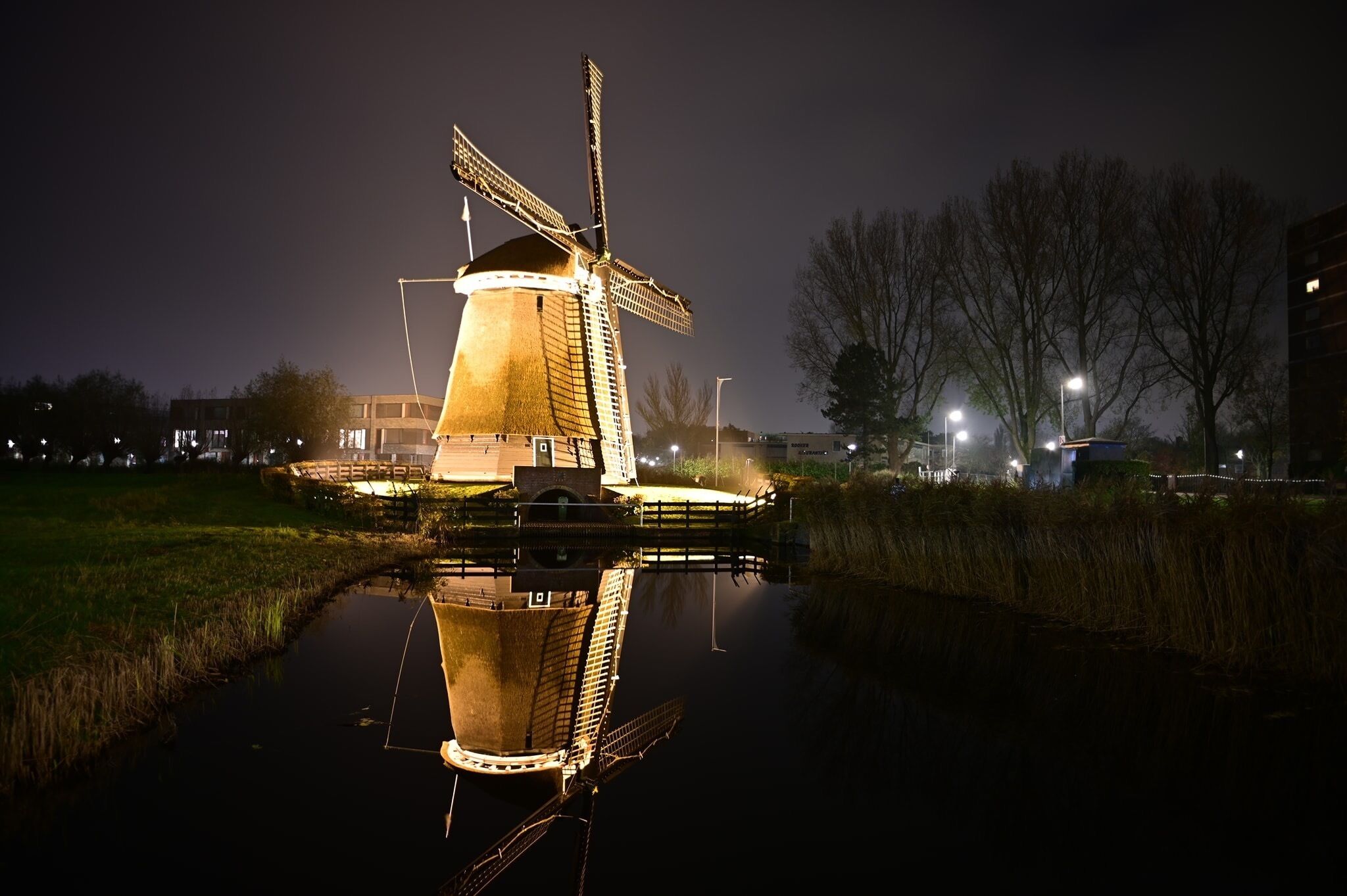 Un moulin à vent la nuit, avec son reflet dans l’eau.