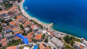 Vue aérienne d’une ville côtière avec une plage, des bâtiments et une flèche bleue pointant vers le bas.
