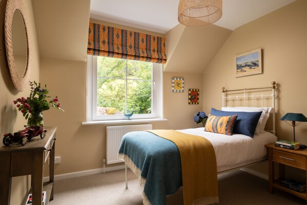A bedroom with a bed, bedside table, lamp, window with curtains, radiator, and a small table with a vase of flowers. - Characterful stone cottage in its own fully enclosed garden. No neighbours! (Kirkcudbright)