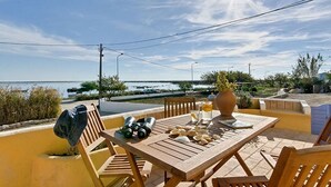 An outdoor patio with a wooden table, chairs, and a view of the sea. - Lovingly renovated Fisherman's cottage « Luazinha » (Tavira)