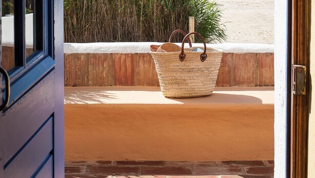 An open door leading to a balcony with a view of the sea, a wicker basket, and a brick wall. - Lovingly renovated Fisherman's cottage « Luazinha » (Tavira)