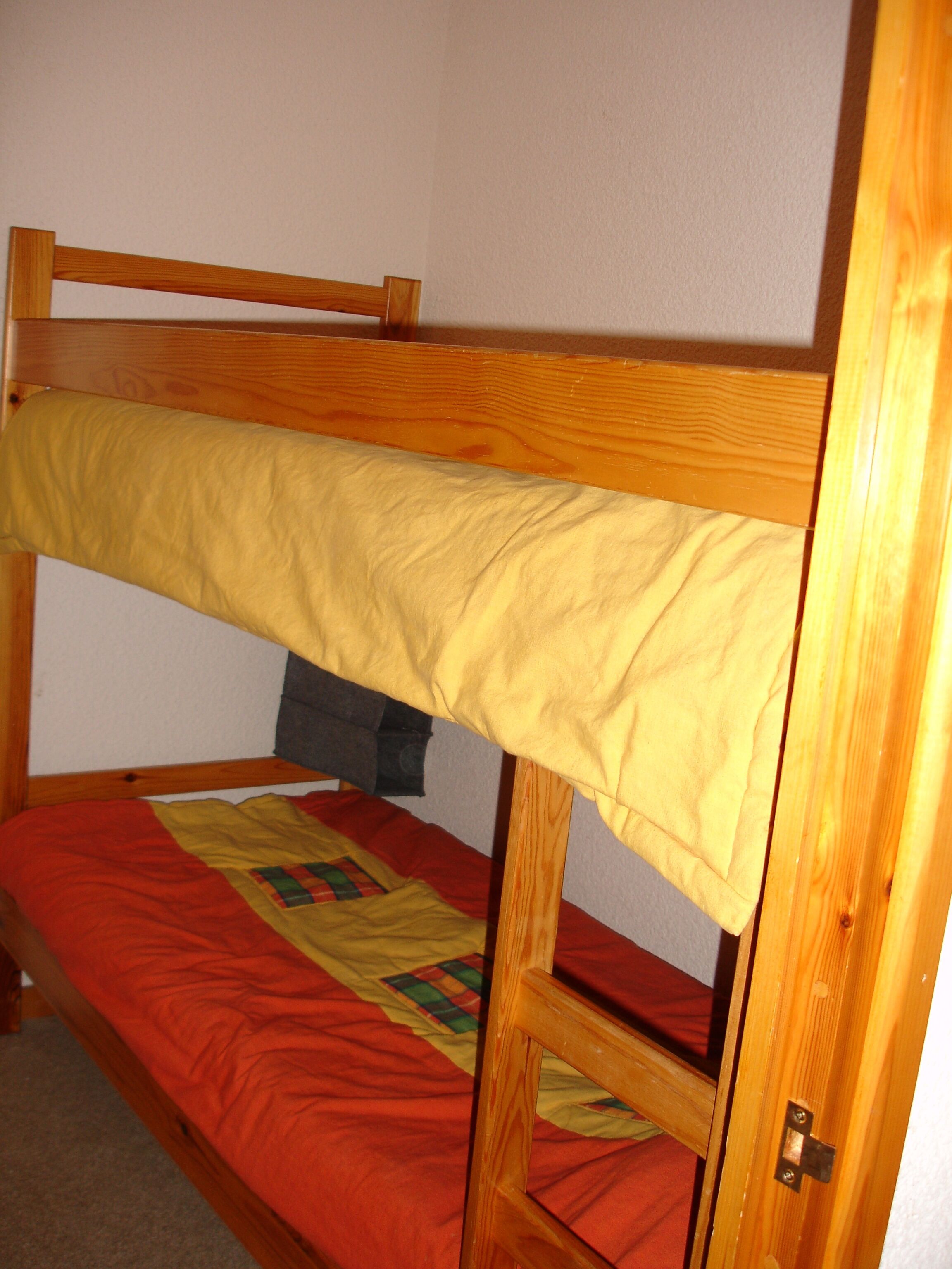 A bunk bed with a wooden frame, a yellow mattress, and a red blanket.