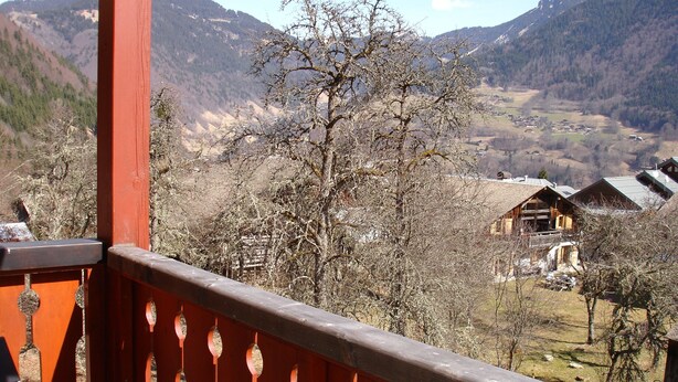 Ein Balkon mit Blick auf eine gebirgige Landschaft, Holzhäuser und einen klaren Himmel.