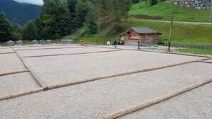 Ein großzügiger Außenbereich mit Kiesboden und Holzbalken, umgeben von Grünpflanzen und einem kleinen Holzhaus.