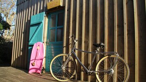 Un vélo est garé devant un bâtiment en bois, dont la porte est bleue, et une enseigne est accrochée au-dessus.