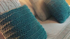 Une pièce chaleureuse avec une tête de lit en bois, un lit recouvert d’une couverture tricotée et agrémenté d’oreillers, et une lampe diffusant une lumière douce.