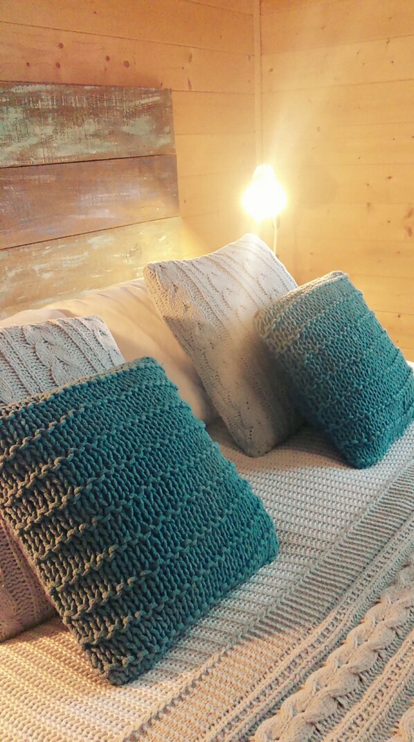 Een gezellige kamer met een houten hoofdbord, een bed met een gebreide deken en kussens, en een lamp die warm licht geeft.