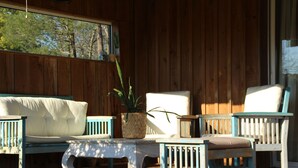 Une terrasse en bois avec un canapé blanc, une chaise bleue et une petite table sur laquelle est posée une plante en pot.