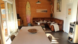 Une pièce chaleureuse avec un décor intérieur en bois, une table à manger avec des chaises, un canapé avec des coussins et une planche de surf appuyée contre le mur.