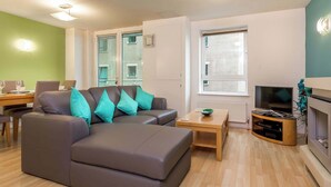 Ein modernes Wohnzimmer mit einem grauen Ecksofa, einem Holztisch, einem Fernseher und einem Kamin.