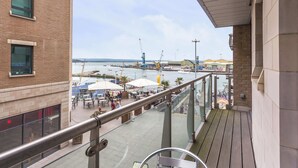 Ein Balkon mit Blick auf einen Hafen, Sitzgelegenheiten im Freien und ein Gebäude mit großen Fenstern.