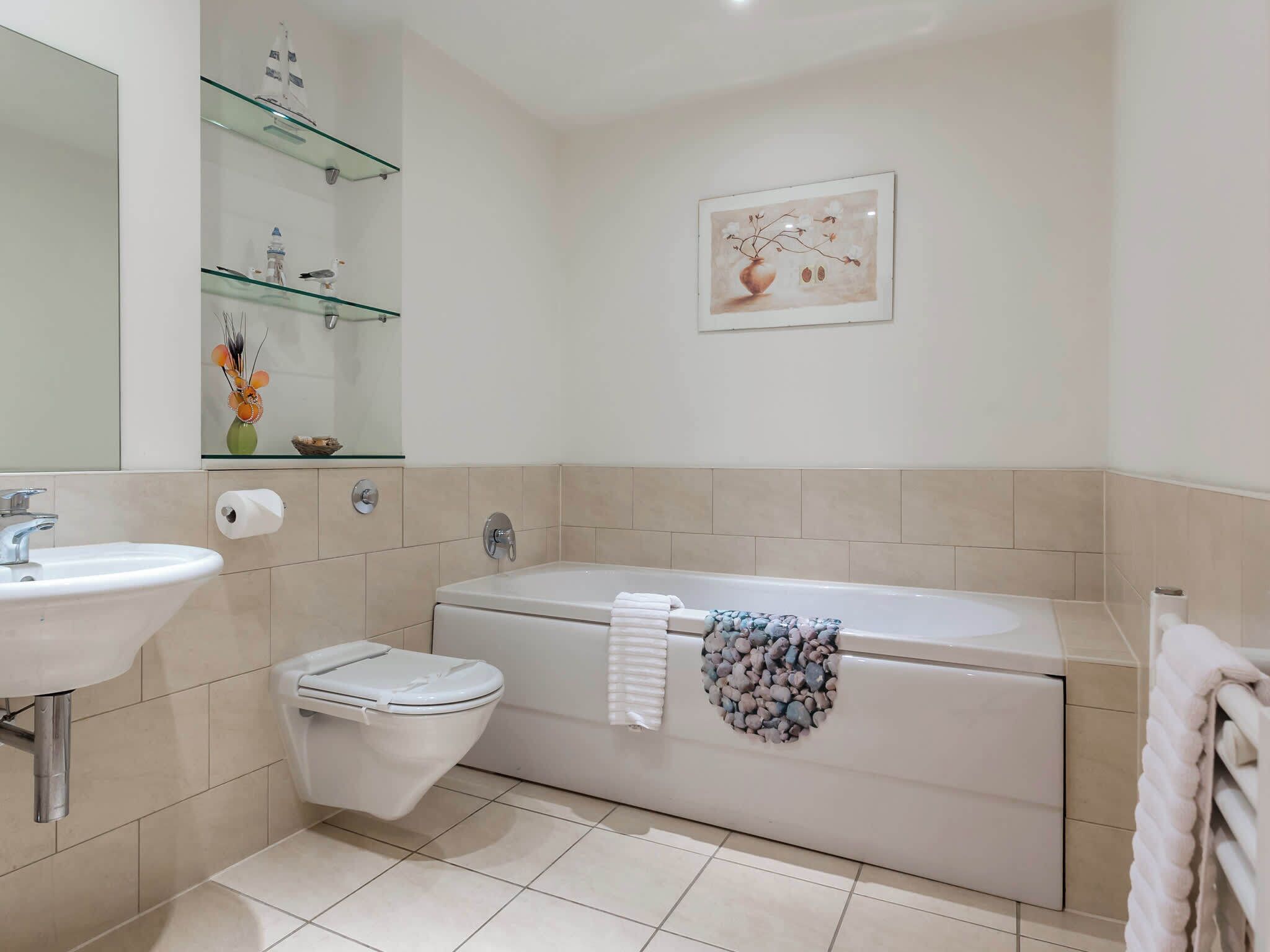 Un bagno con lavandino, WC e vasca da bagno. Ci sono scaffali sopra il lavandino e un quadro appeso al muro.