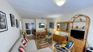 Ein Wohnzimmer mit einer Couch, Sesseln, einem Fernseher und einem Essbereich mit Tisch und Stühlen.