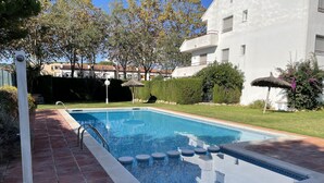 Ein rechteckiger Pool mit Fliesenränder, einer Metallleiter und einem Reetdach-Sonnenschirm.
