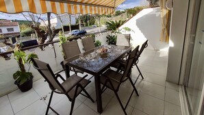 Ein Balkon mit gestreiftem Sonnenschirm, einem Tisch mit Stühlen, Topfpflanzen und Blick auf die Straße und Häuser.