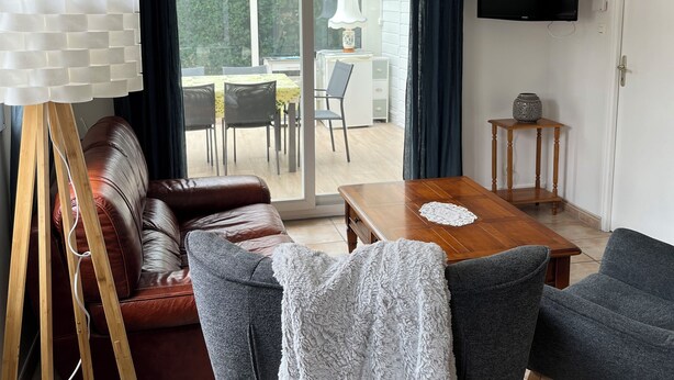 Un salon moderne avec un canapé, des fauteuils, une table basse en bois et un téléviseur.