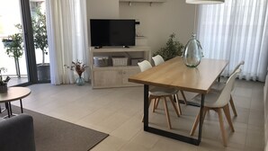 A modern living room with a wooden dining table, white chairs, a flat-screen TV, a sofa, and a coffee table. - BALMINS APARTMENT, FULLY EQUIPPED 50 MTS FROM THE BEACH OF ST.SEBASTIA (SITGES)
