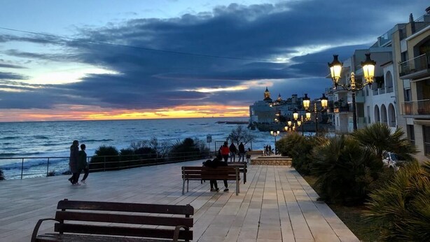 A waterfront promenade with benches and street lamps, overlooking the sea and a historic building. - BALMINS APARTMENT, FULLY EQUIPPED 50 MTS FROM THE BEACH OF ST.SEBASTIA (SITGES)