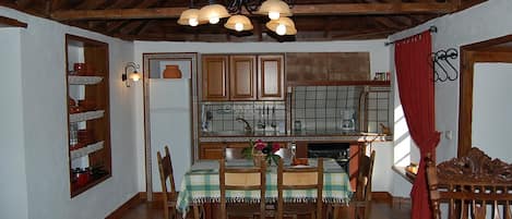 Un comedor con una mesa de madera, sillas, una lámpara de araña y una cocina al fondo.