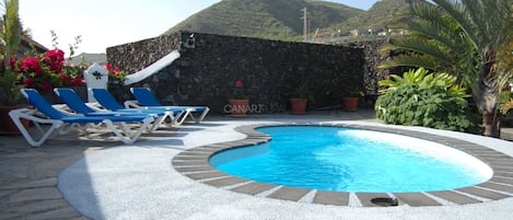 A swimming pool with lounge chairs, surrounded by a stone wall and potted plants.