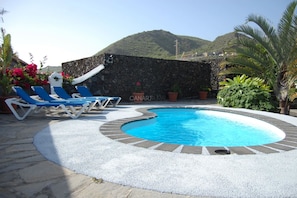 A swimming pool with lounge chairs, surrounded by a stone wall and potted plants.