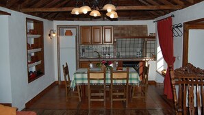 Zona de menjador amb taula de fusta, cadires, un penjallum i una cuina al fons.