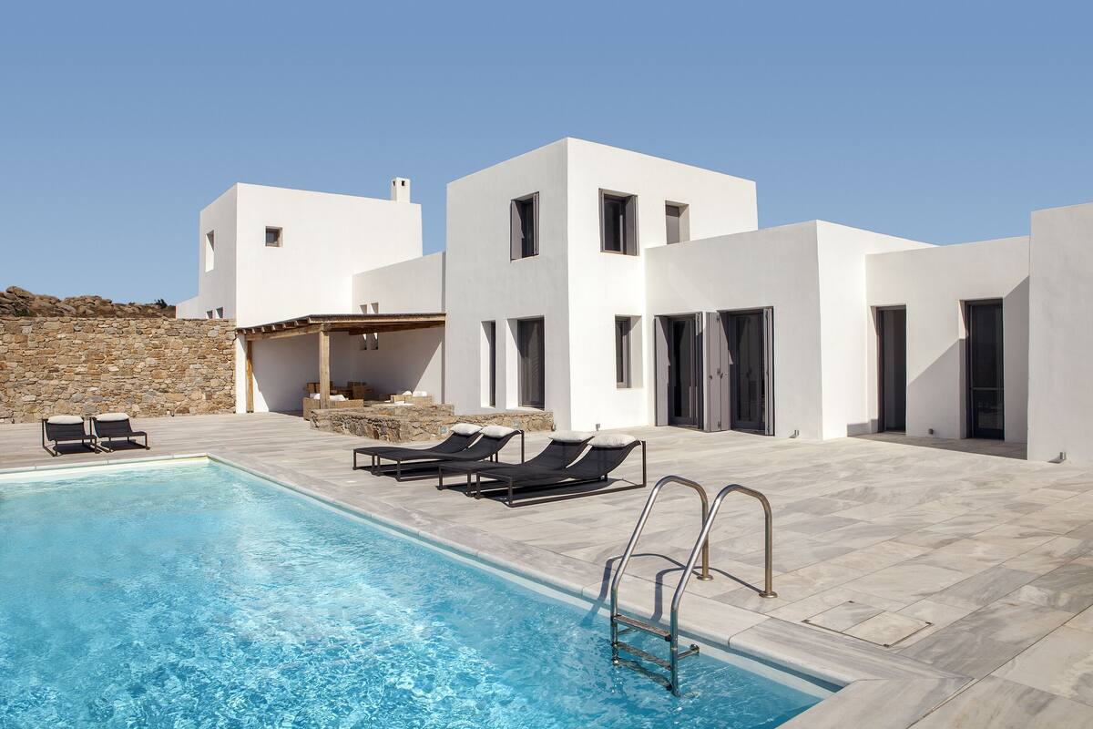 A modern pool area with a clear blue pool, black lounge chairs, and a stone wall.