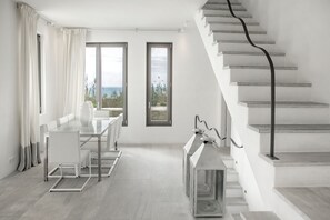 A modern, minimalist room with a dining area, large windows, and a staircase.