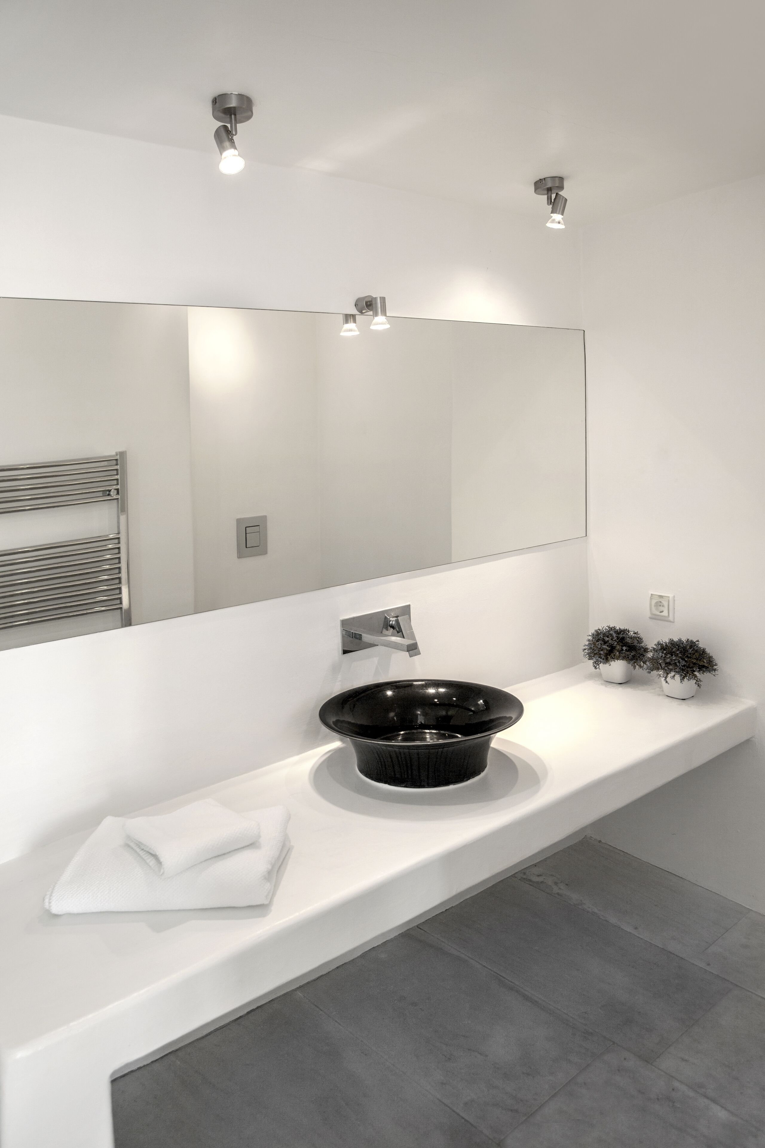 Une salle de bain moderne avec un meuble-lavabo blanc, un lavabo noir et un grand miroir.