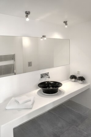 A modern bathroom with a white vanity, a black sink, and a large mirror. - New Liberation Villas (Mykonos)