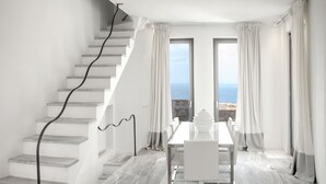 A modern interior with a staircase, a dining area, and large windows offering a view of the sea. - New Liberation Villas (Mykonos)