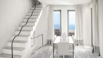 Un interior moderno con una escalera, una zona de comedor y ventanas amplias que ofrecen vista al mar.