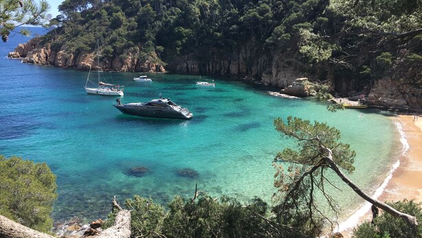 Uma área costeira com águas turquesa cristalinas, barcos e um litoral rochoso.