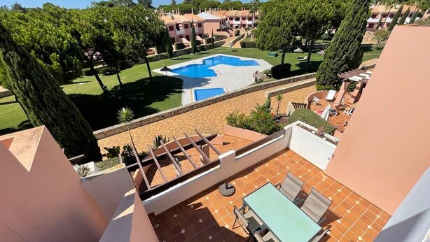Eine Dachterrasse mit Pool, Sitzgelegenheiten im Freien und Blick auf die umliegenden Gebäude und die grüne Umgebung.