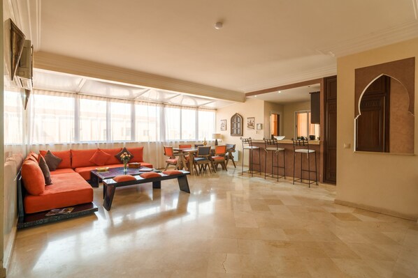 A spacious living room with a large orange sofa, a coffee table, and a dining area with chairs and a table.