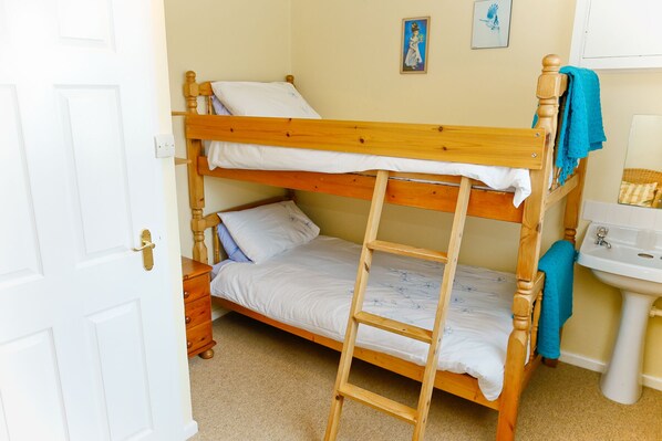 Una cama individual superpuesta con escalera, una mesita de noche, un cajón pequeño y una repisa de pared.