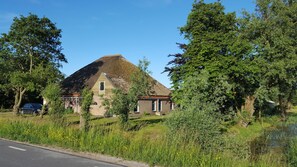 A traditional house with a steep roof, surrounded by lush greenery and a small stream. - Holiday home Het Vosgen, farmhouse between the bulb fields near the sea (St. Maartensbrug)