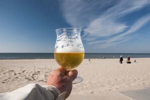 A hand holding a glass of beer with a beach and ocean in the background. - Holiday home Het Vosgen, farmhouse between the bulb fields near the sea (St. Maartensbrug)
