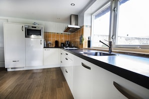 A modern kitchen with white cabinets, a built-in oven, a coffee maker, and a window with a view of the outside. - Holiday home Het Vosgen, farmhouse between the bulb fields near the sea (St. Maartensbrug)