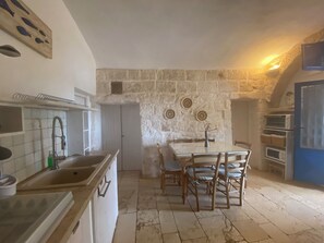 Una cocina con pared de piedra, una mesa de comedor con sillas, un fregadero y un horno empotrado.
