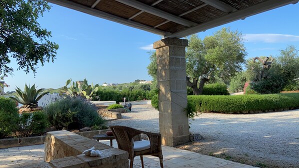 A covered outdoor seating area with a stone pillar, a wicker chair, and a table.