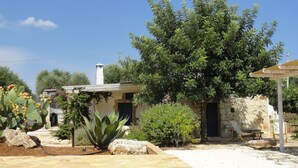 A stone house with a tiled patio, surrounded by greenery and a clear blue sky. - Wonderful "Trullo Saraceno" (Ostuni)