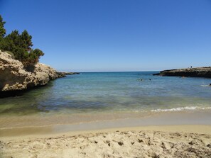 A beach with clear water, sandy shore, and rocky cliffs.