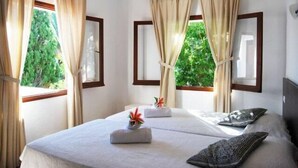 Habitación de hotel con dos camas, cortinas color beige y vista a áreas verdes.