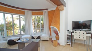 Una sala de estar con un sofá, una mesa de centro, un televisor y un escritorio con una silla.