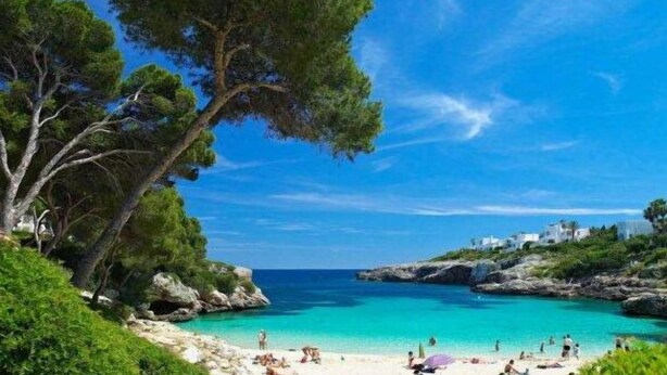 Escena costera de una playa con aguas turquesas cristalinas, afloramientos rocosos y vegetación exuberante.