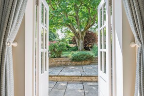 An open doorway leading to a stone-paved garden with a large tree and various shrubs. - Stunning 16th Century Cotswold Manor House, Sleeps 12-14. (Chipping Norton)