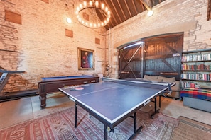 Una habitación con mesa de ping pong, mesa de billar, estantería y un cuadro en la pared.